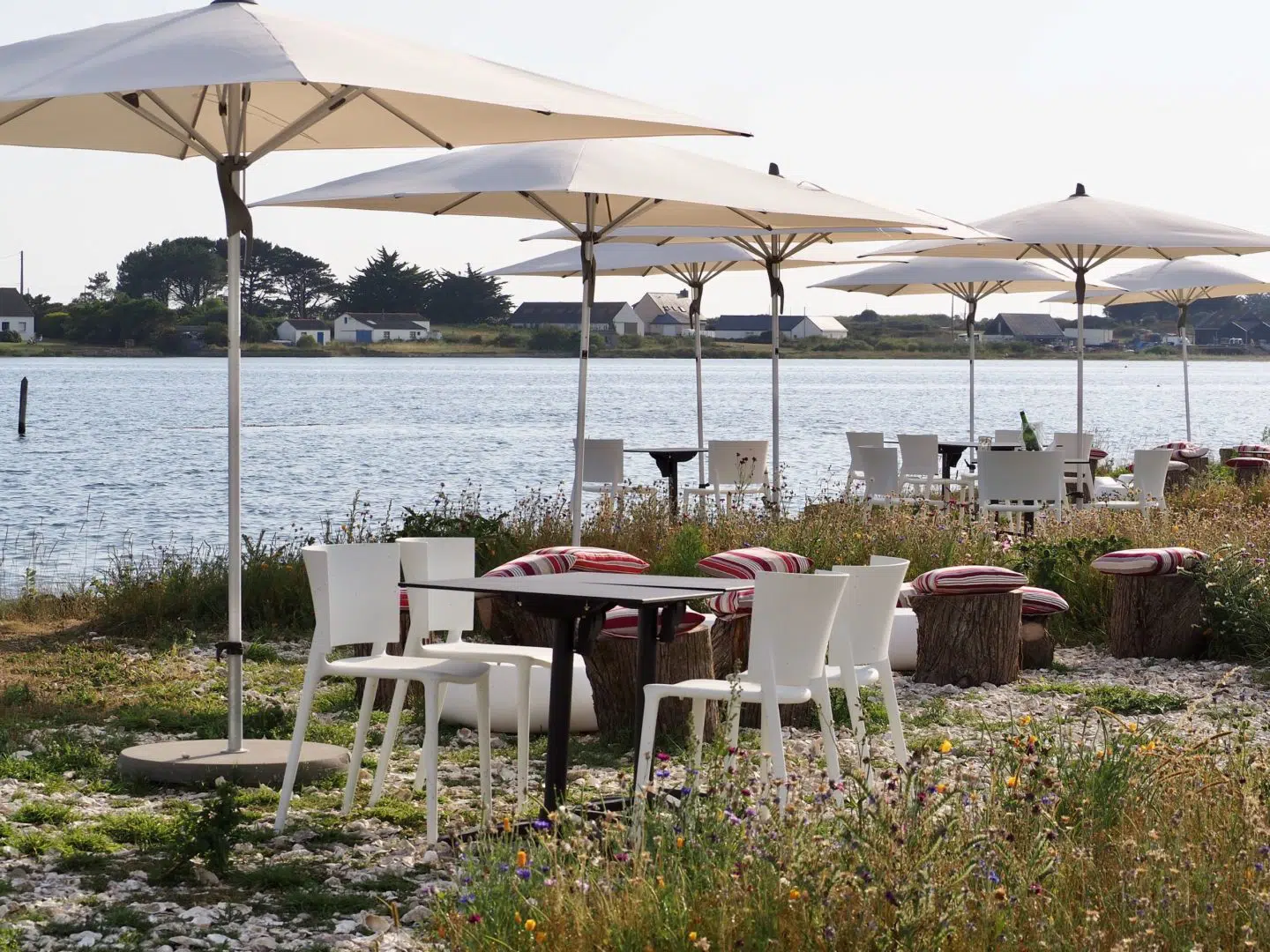 Terrasse au bord de l’eau avec tables et parasols.
